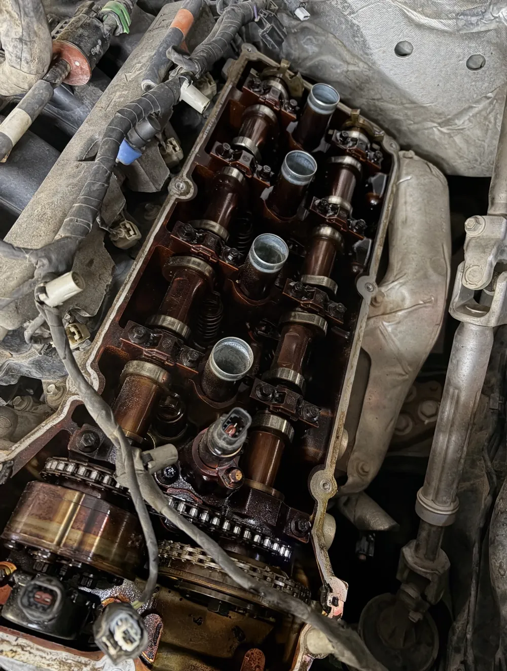 Motor con la tapa de válvulas quitada, con los árboles de levas y la culata cubiertos de residuo de aceite oscuro y quemado